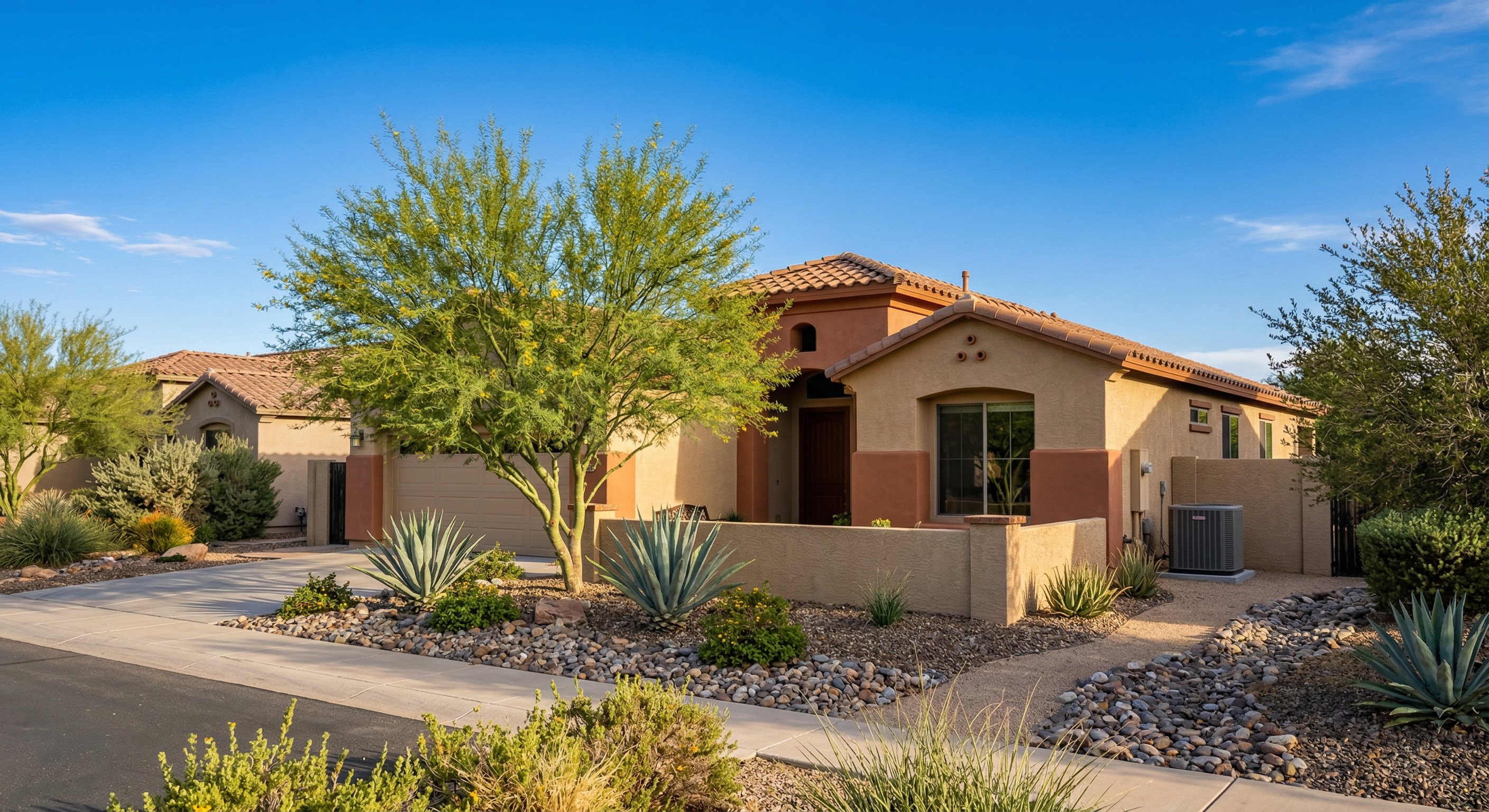 Stucco home in Chandler, AZ with properly installed AC condenser unit on side of house, desert landscaping with river rock and agave plants, clear blue Arizona sky