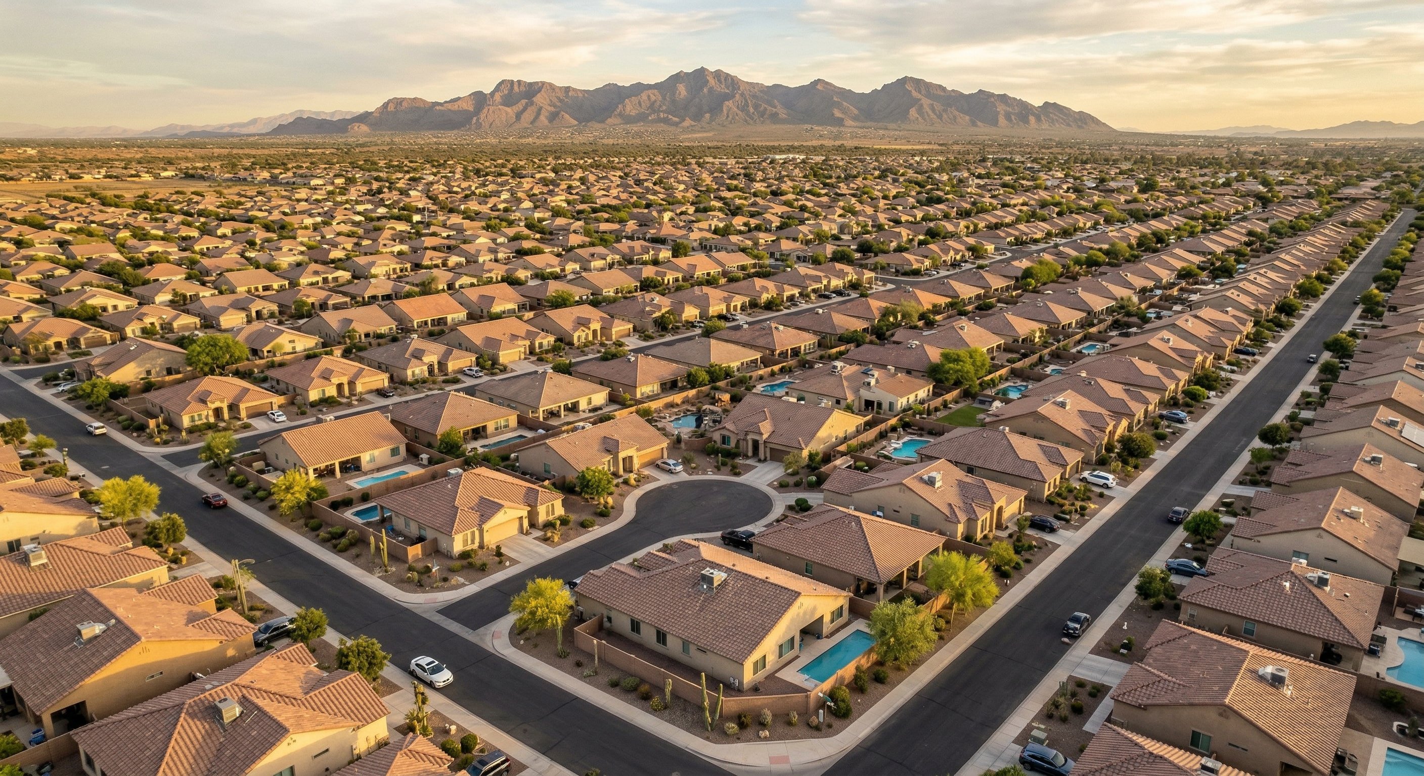 Bird's eye view of a flat-roof Arizona stucco home in a Surprise AZ subdivision, showing a rooftop HVAC package unit, solar panels, desert landscaping with gravel yards, and Estrella Mountain range visible in the distance