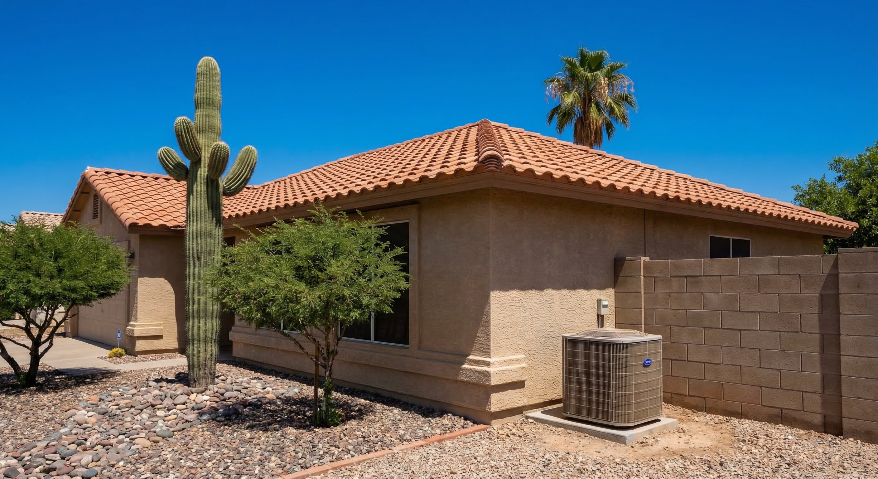 Desert landscaping in front of a tan stucco Mesa, Arizona home with AC condenser unit on a concrete pad next to the garage